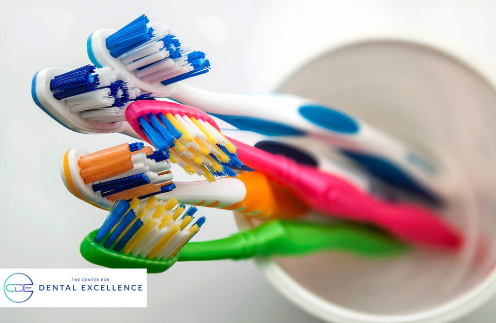 A cup holding multiple toothbrushes of various colors and sizes, representing different family members — toddler, child, teen, and adult — each with their own toothbrush for personal oral care.